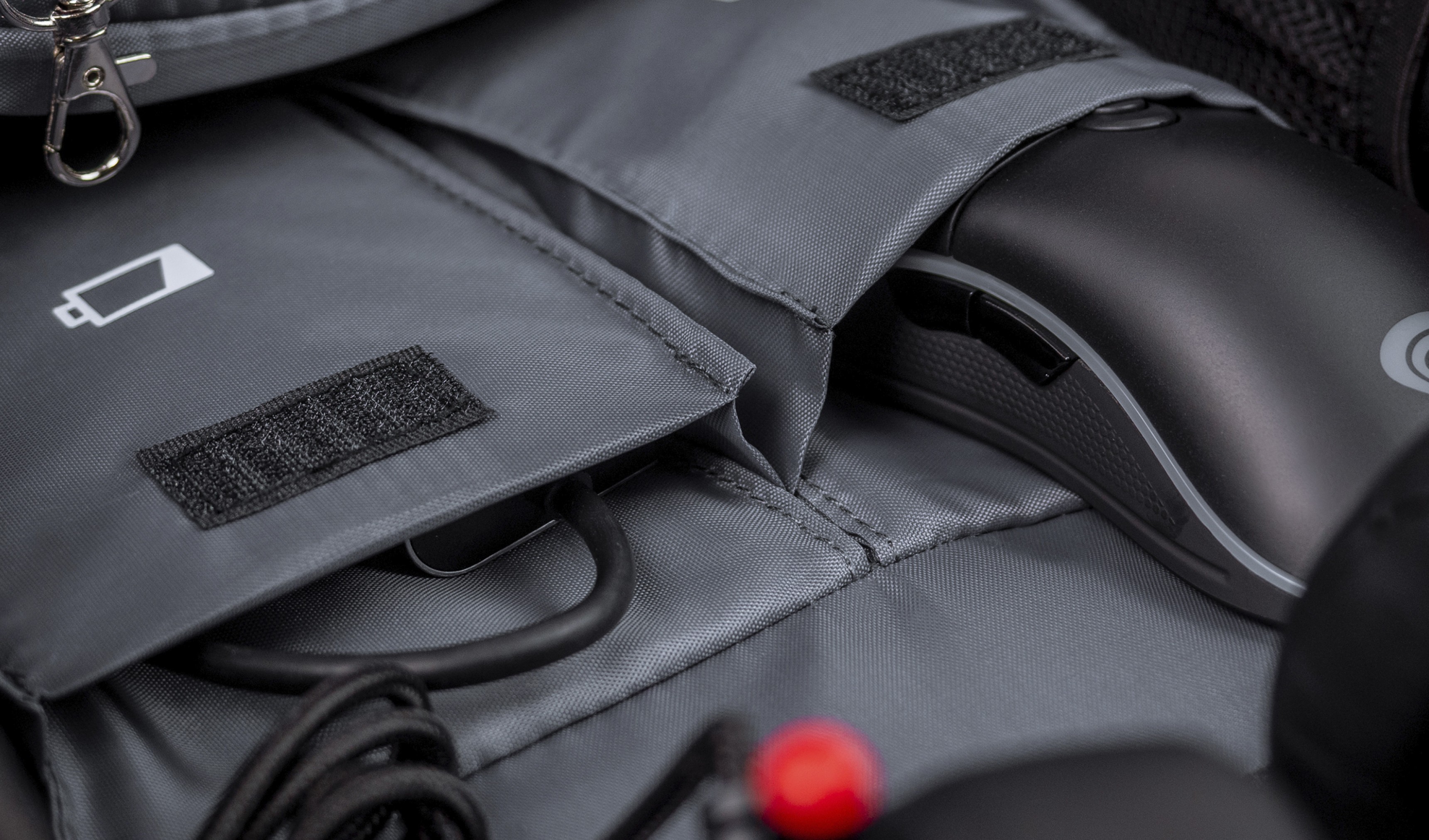 Grauer Innenraum des Genesis Pallad 550 Rucksacks mit Fächern für eine Maus und Kabel, mit einem Batteriesymbol