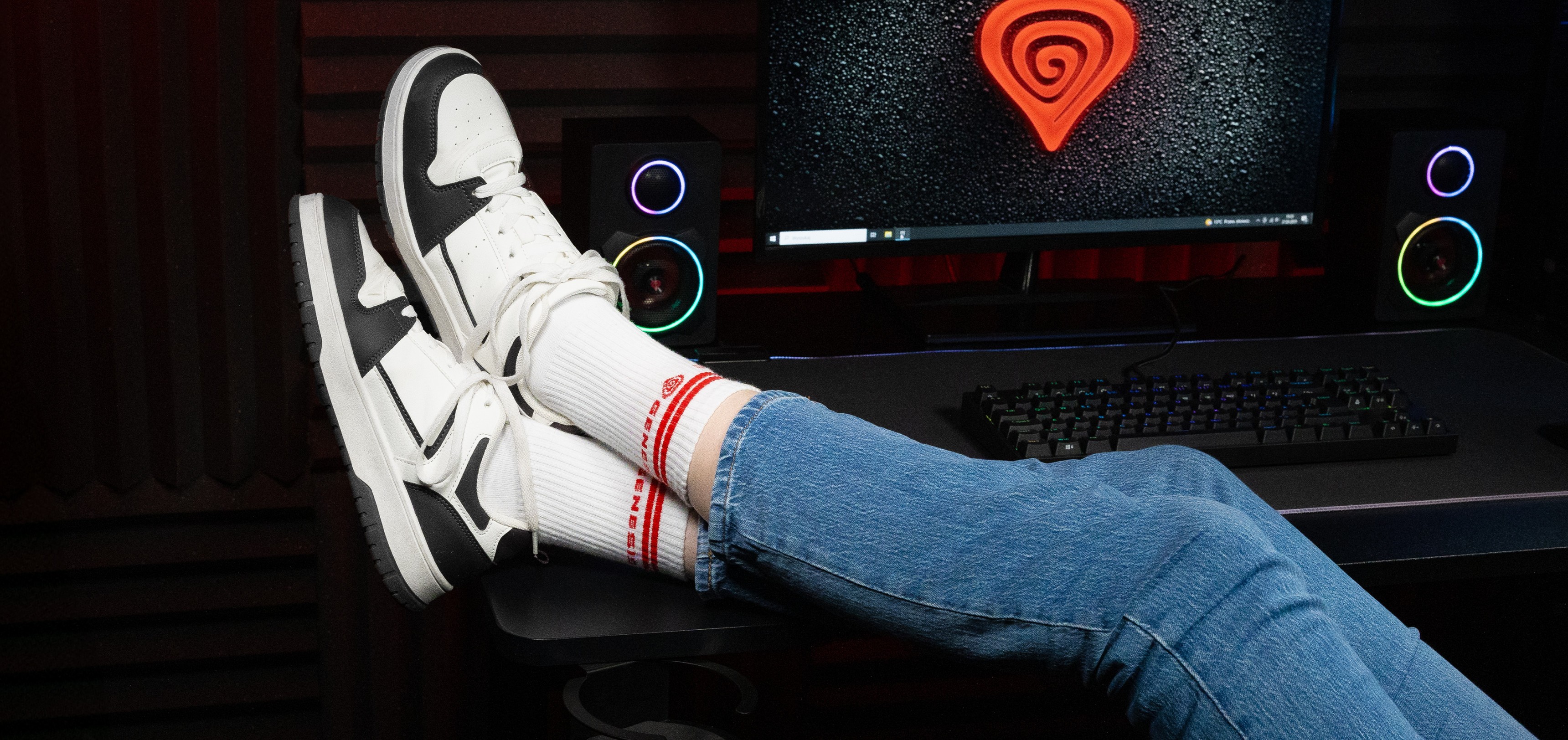Sportliche Socken in Weiß mit roten Streifen, getragen mit stylischen Sneakern, und blaue Jeans vor einem Computer-Hintergrund